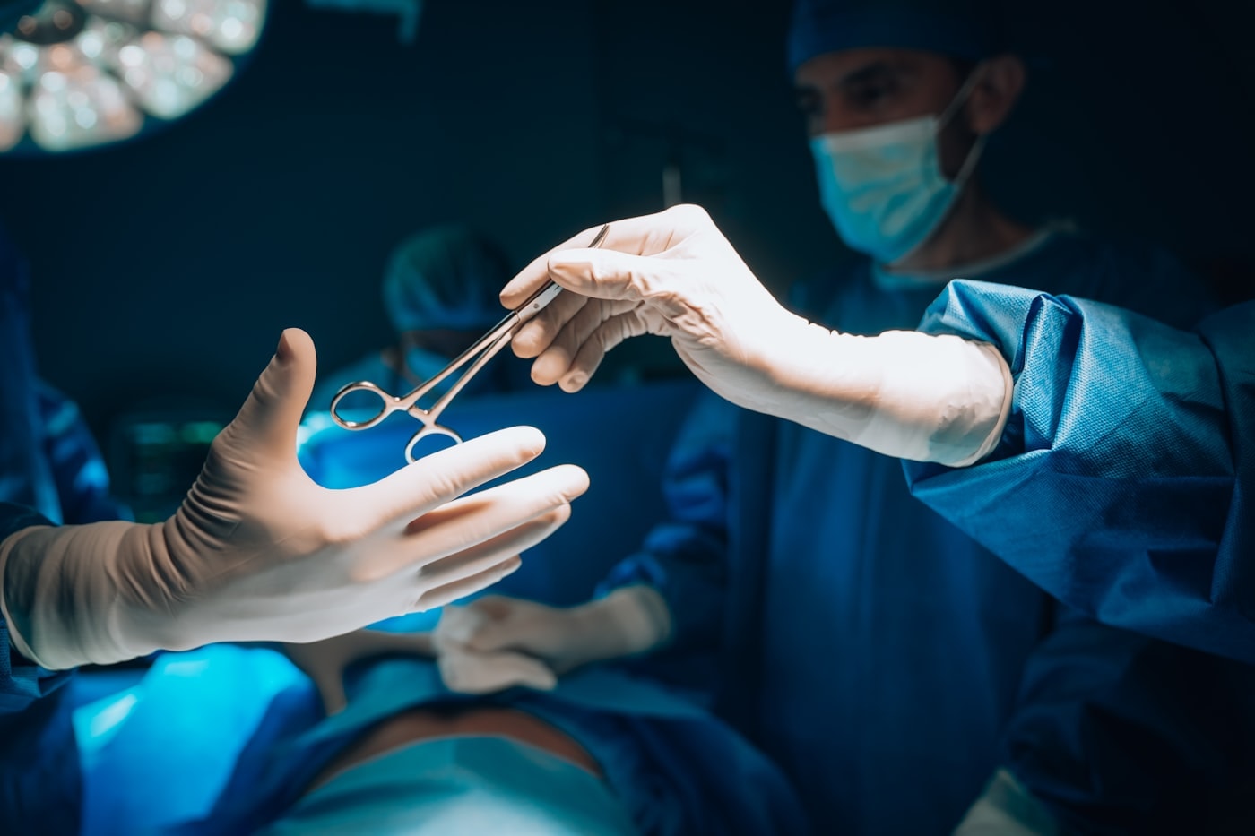 A gloved hand passing surgical scissors to another during an operation