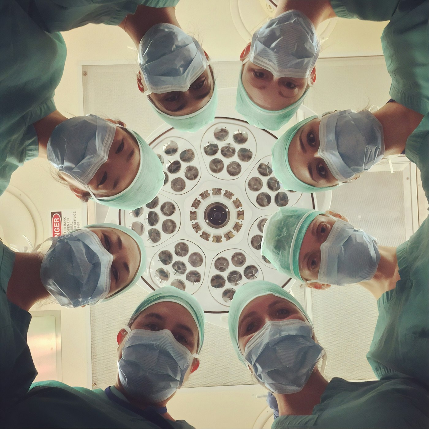 Masked theatre team looking down beneath the operating light