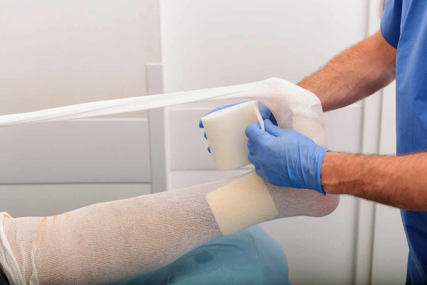 Gloved hands applying a gauze dressing to a patient’s leg